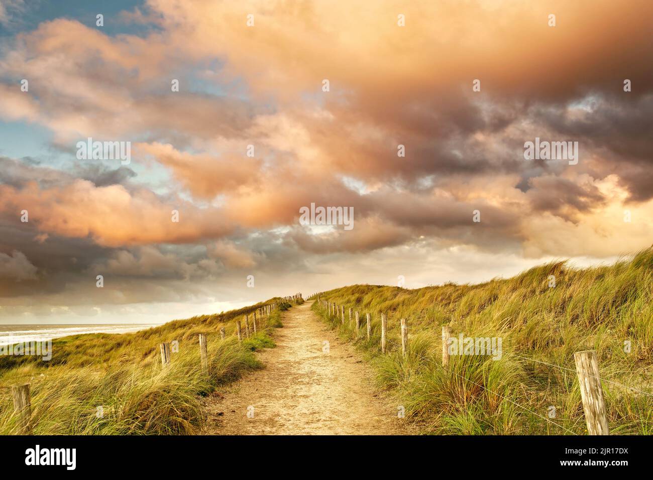 A beautiful sandy path along the ocean. The morning sun is illuminating some clouds. North