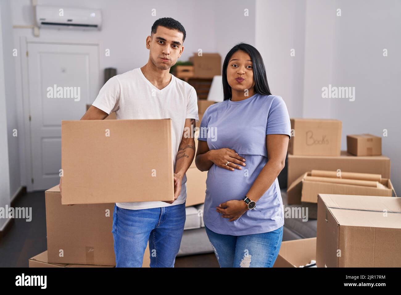 Young hispanic couple expecting a baby moving to a new home puffing ...