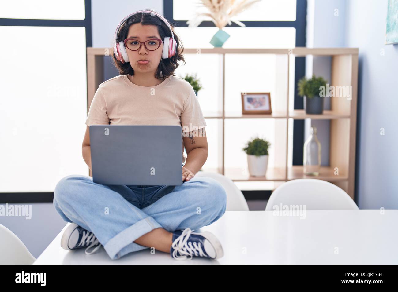 Young hispanic woman using laptop sitting on the table wearing ...