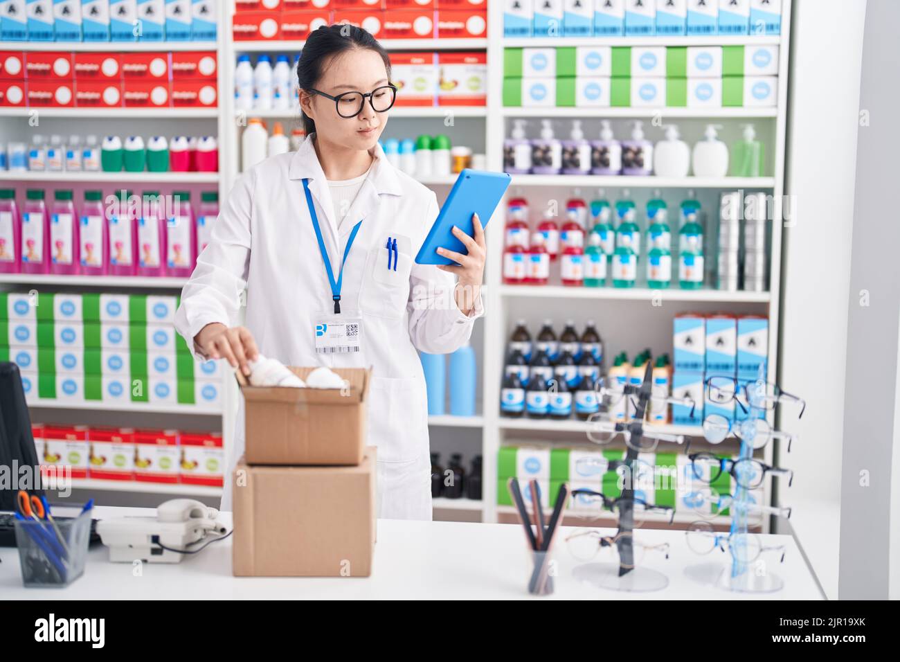 Young chinese woman pharmacist using touchpad holding pills bottle at ...