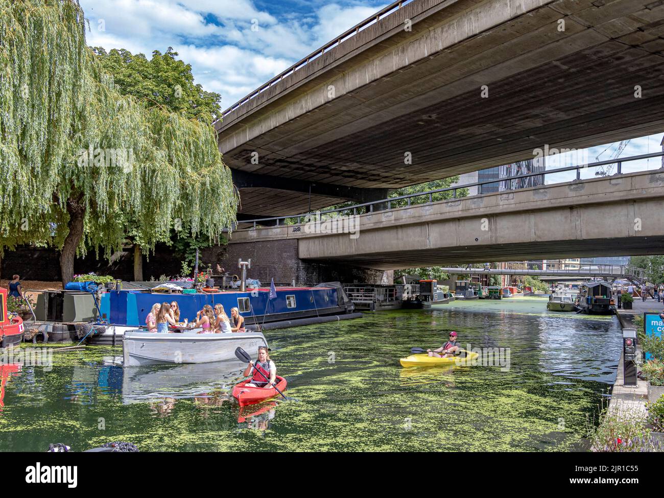 People in kayaks and a group of girl in a boat passing under the Westway on the Paddington arm of the Grand Union Canal , Paddington ,London, W2 Stock Photo