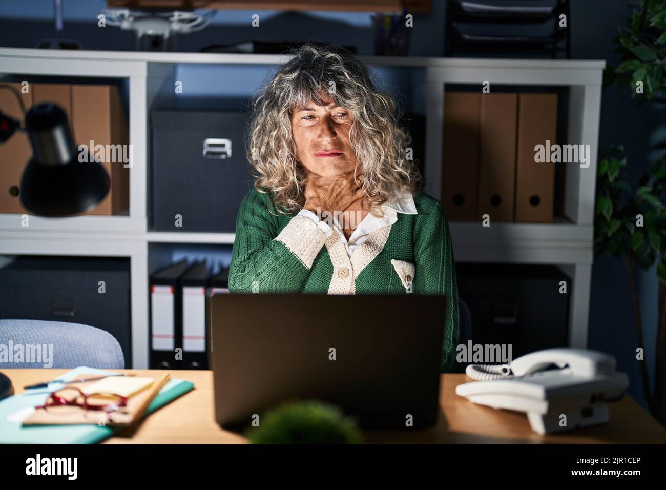 Middle age woman working at night using computer laptop touching ...