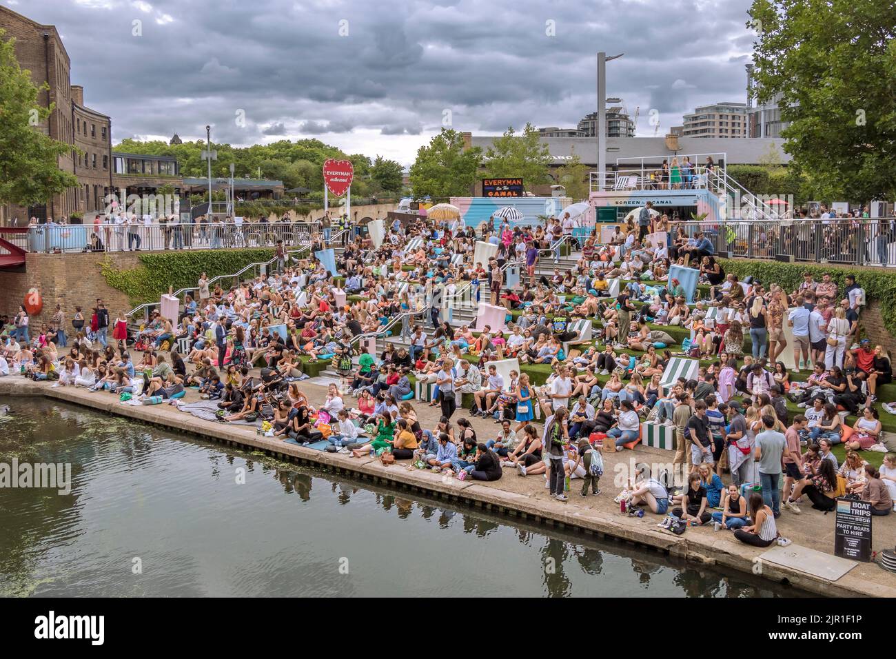 Crowds of people sitting on the canalside steps on the Regent's canal near Granary Square at Kings Cross on a warm summers evening , London Stock Photo