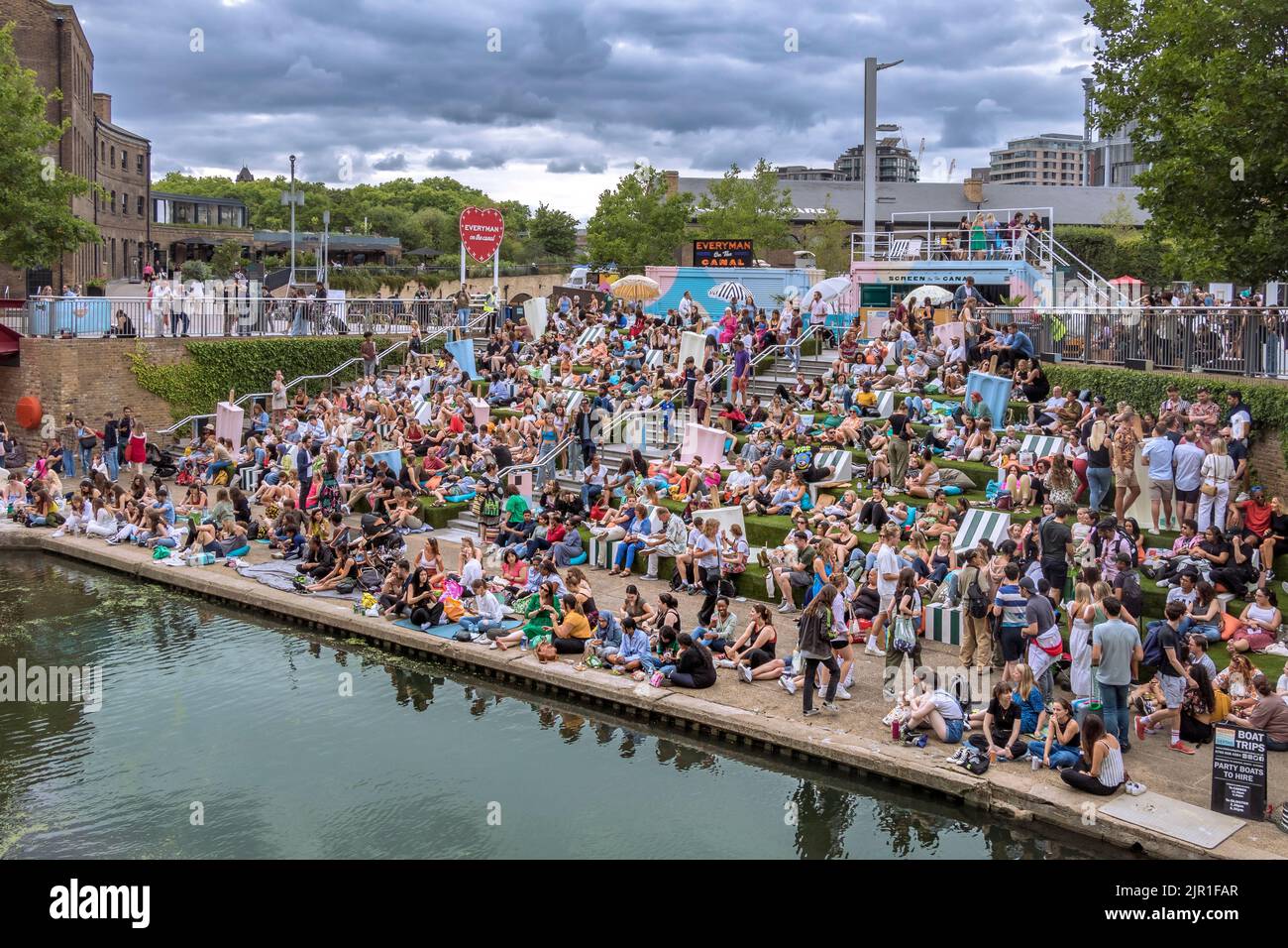 Crowds of people sitting on the canalside steps on the Regent's canal near Granary Square at Kings Cross on a warm summers evening , London Stock Photo