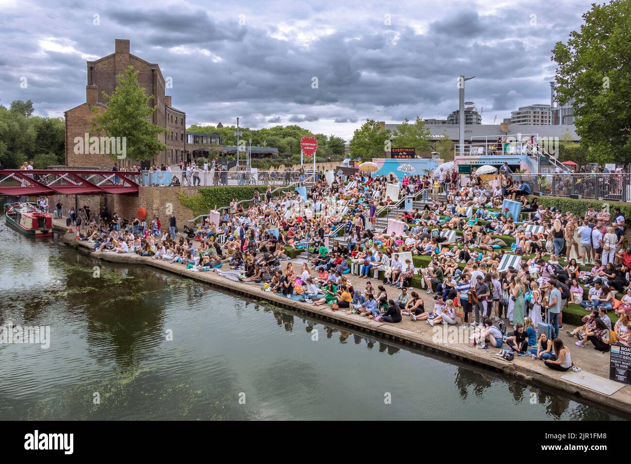 Crowds of people sitting on the canalside steps on the Regent's canal near Granary Square at Kings Cross on a warm summers evening , London Stock Photo