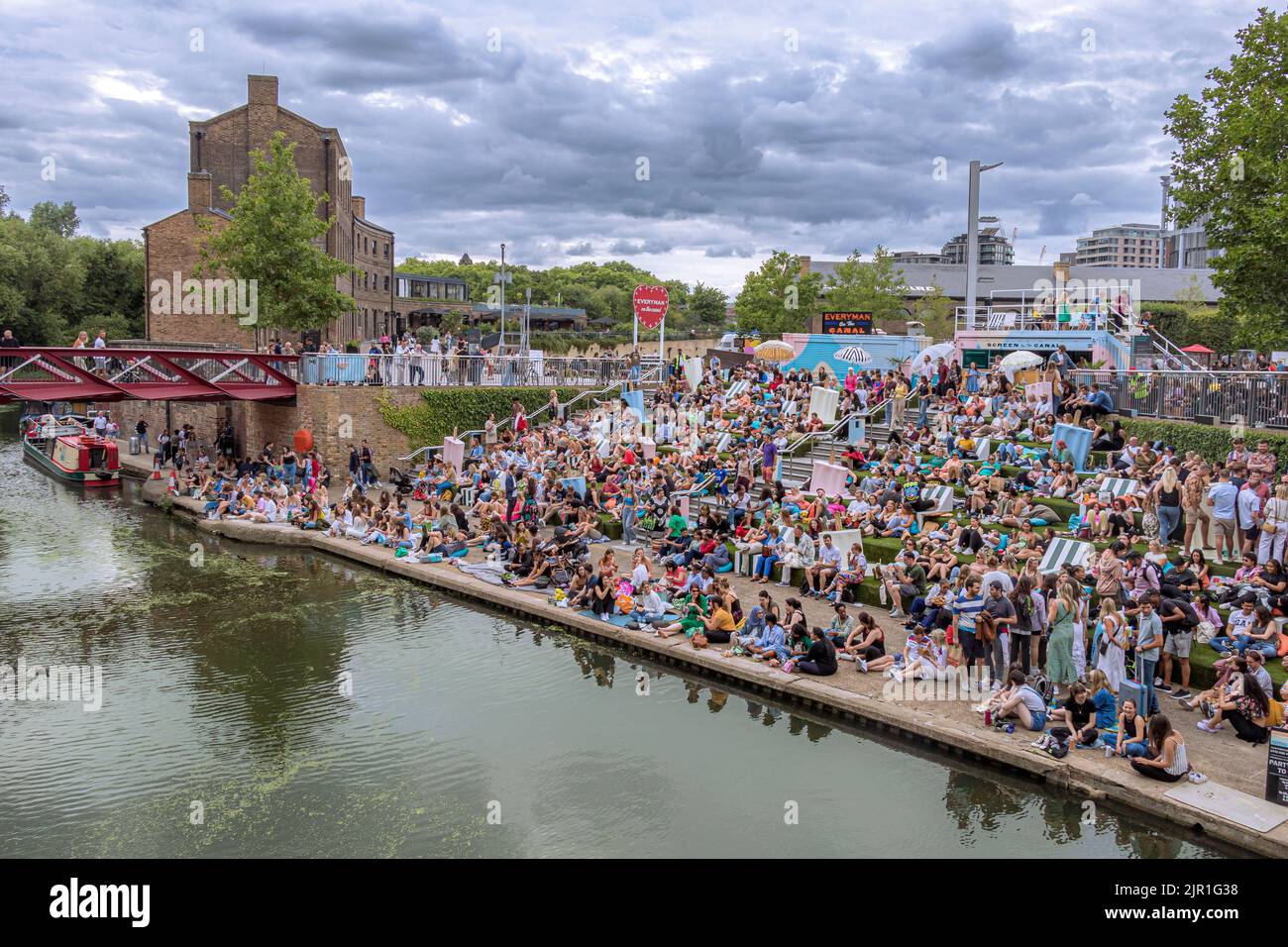 Crowds of people sitting on the canalside steps on the Regent's canal near Granary Square at Kings Cross on a warm summers evening , London Stock Photo