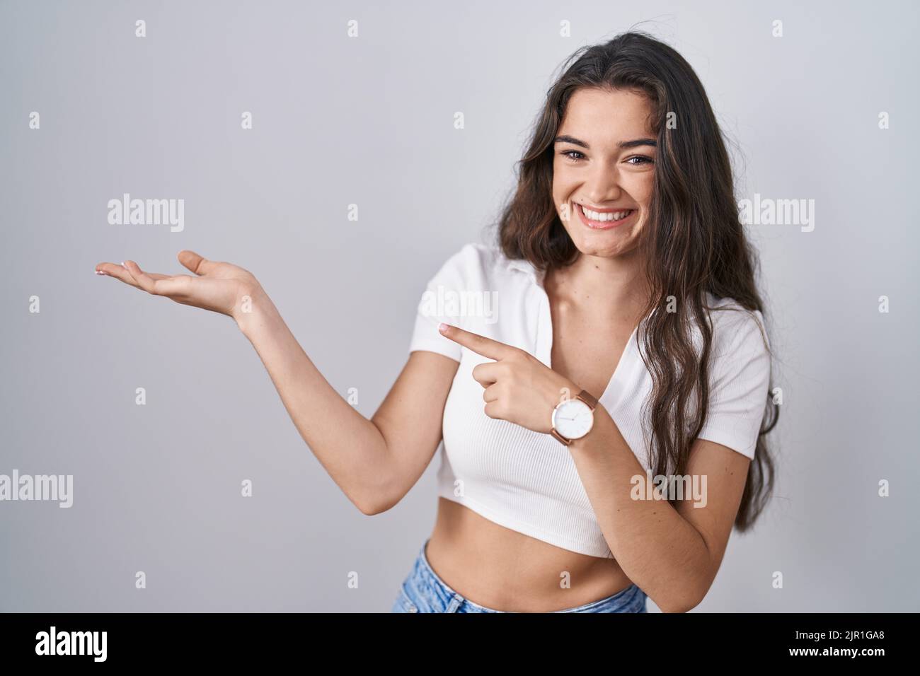 Young teenager girl standing over white background amazed and smiling to the camera while presenting with hand and pointing with finger. Stock Photo