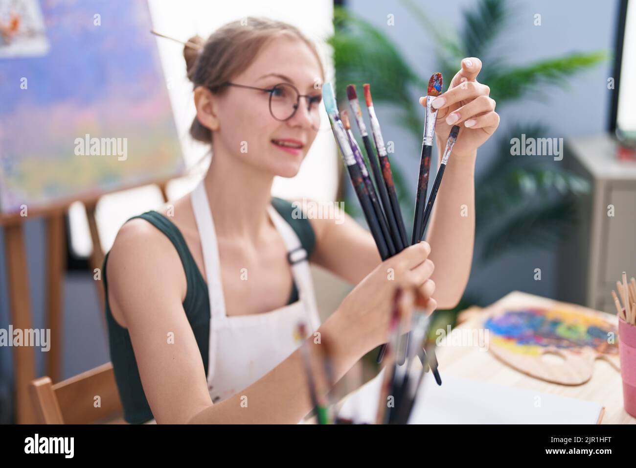 Young caucasian woman artist smiling confident holding paintbrushes at ...