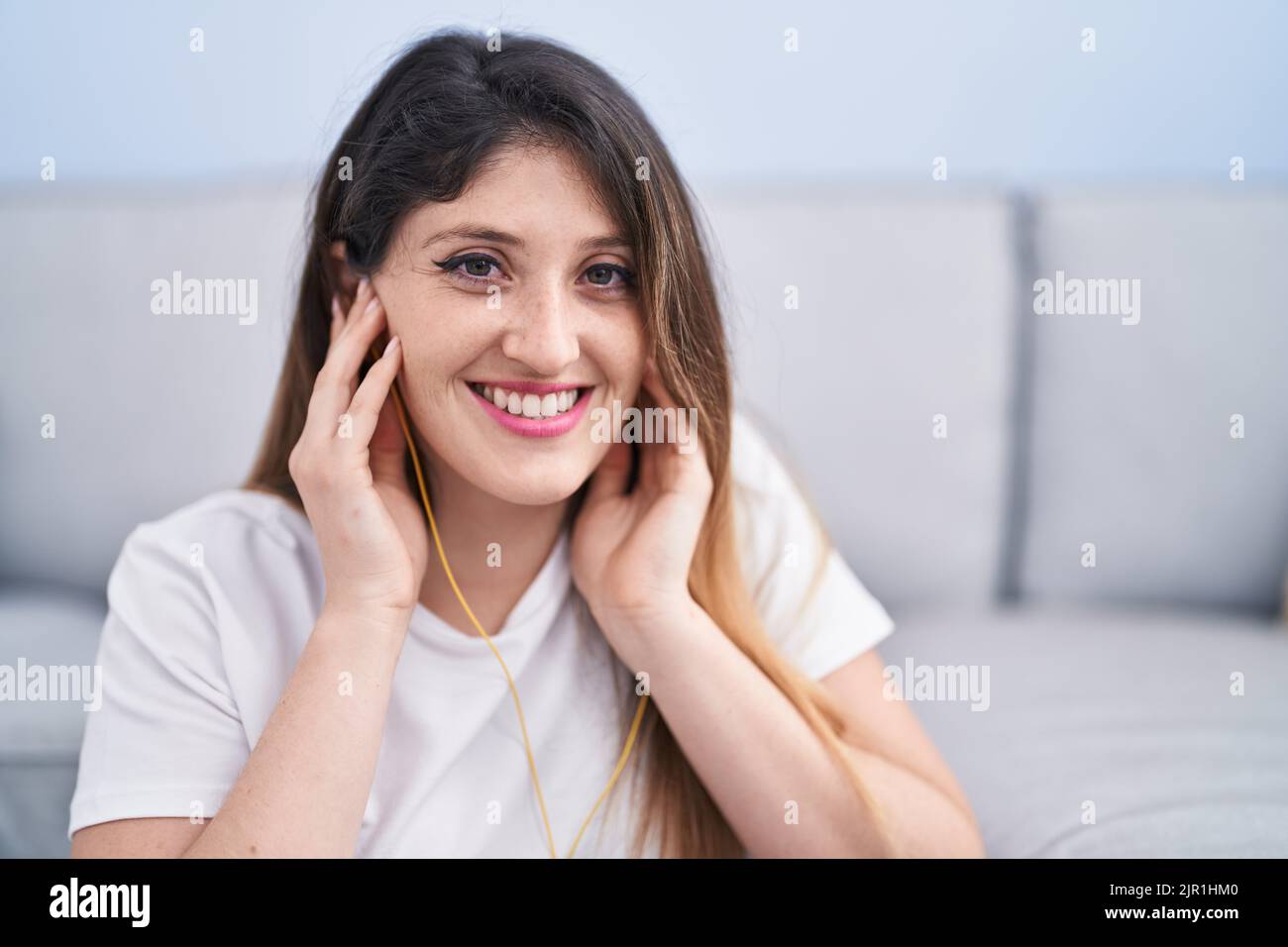Young hispanic woman listening to music sitting on floor at home Stock ...