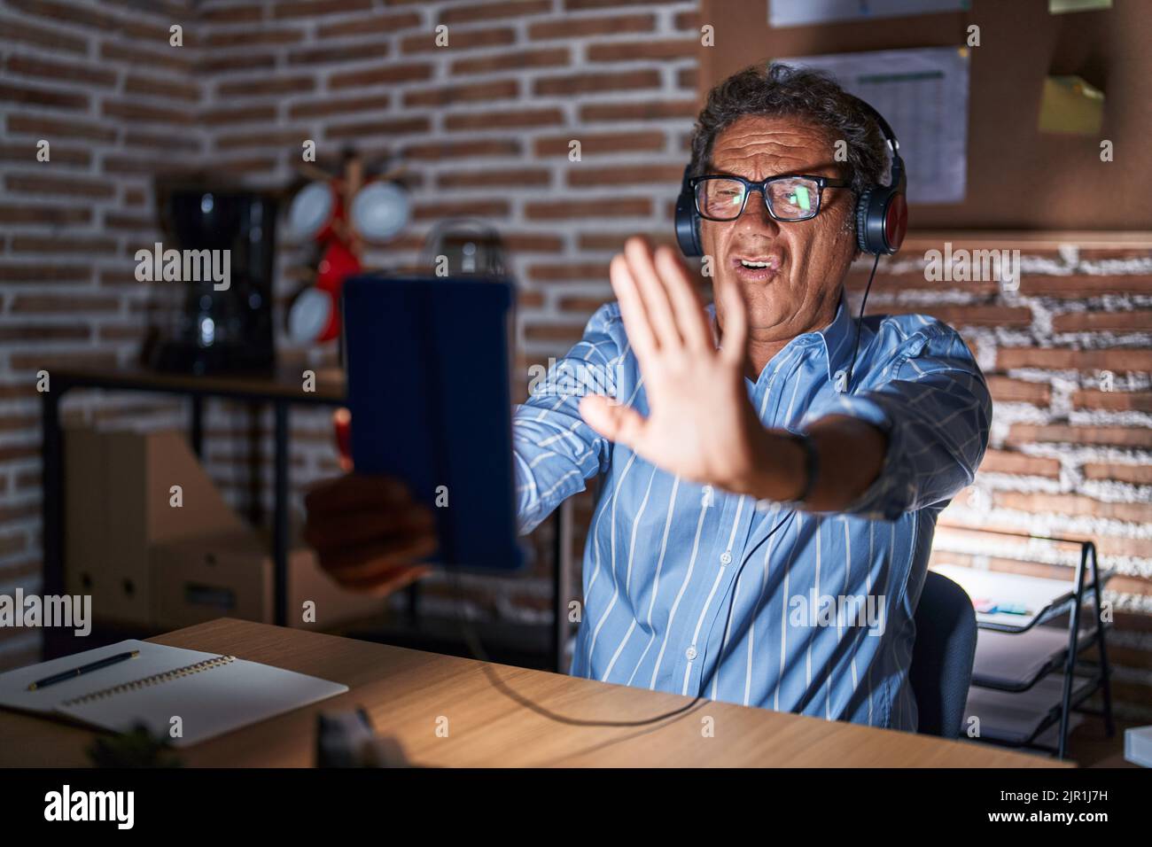 Middle age hispanic man using touchpad sitting on the table at night doing stop gesture with hands palms, angry and frustration expression Stock Photo