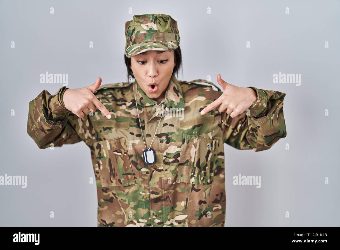 Young south asian woman wearing camouflage army uniform pointing down with fingers showing advertisement, surprised face and open mouth Stock Photo