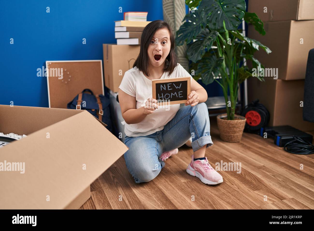 Hispanic girl with down syndrome sitting on the floor at new home angry and mad screaming frustrated and furious, shouting with anger. rage and aggres Stock Photo
