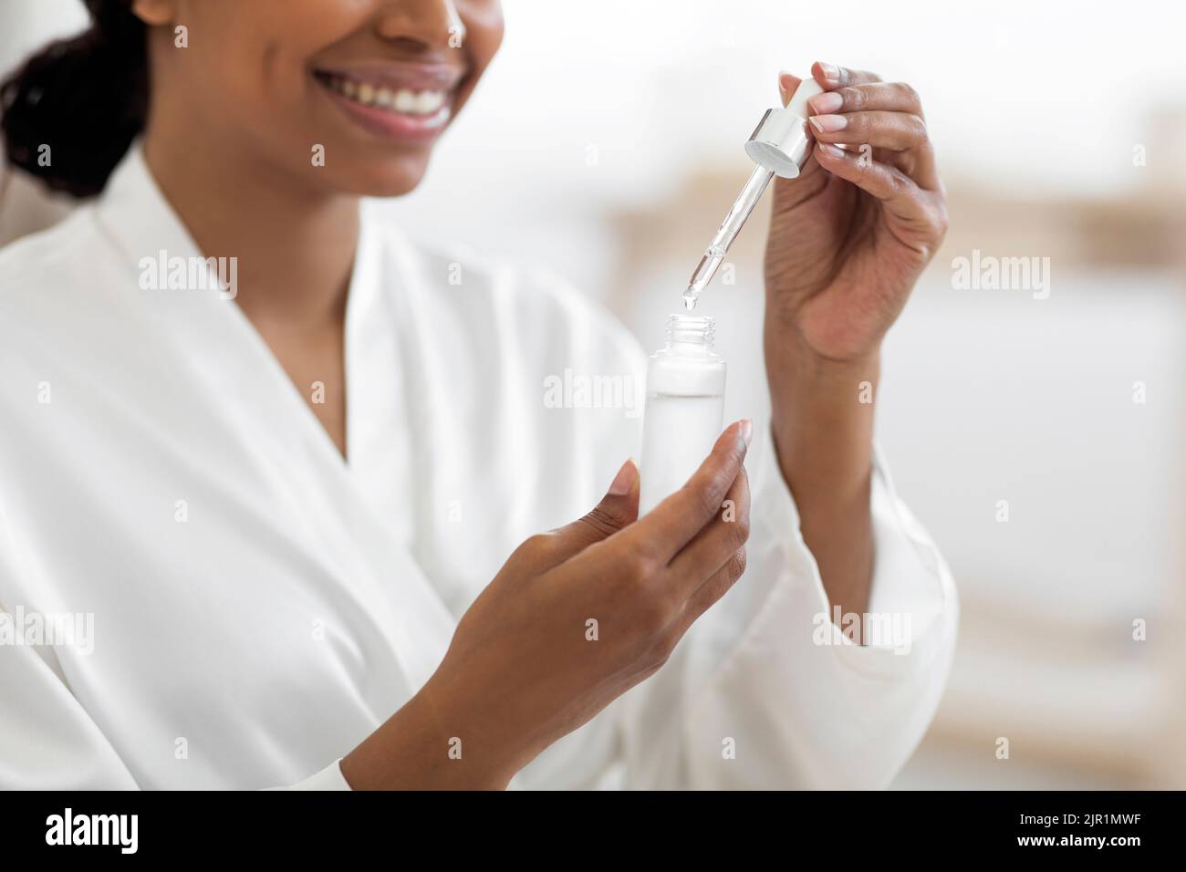 Smiling Black Woman Using Moisturizing Serum While Making Beauty Treatments At Home Stock Photo