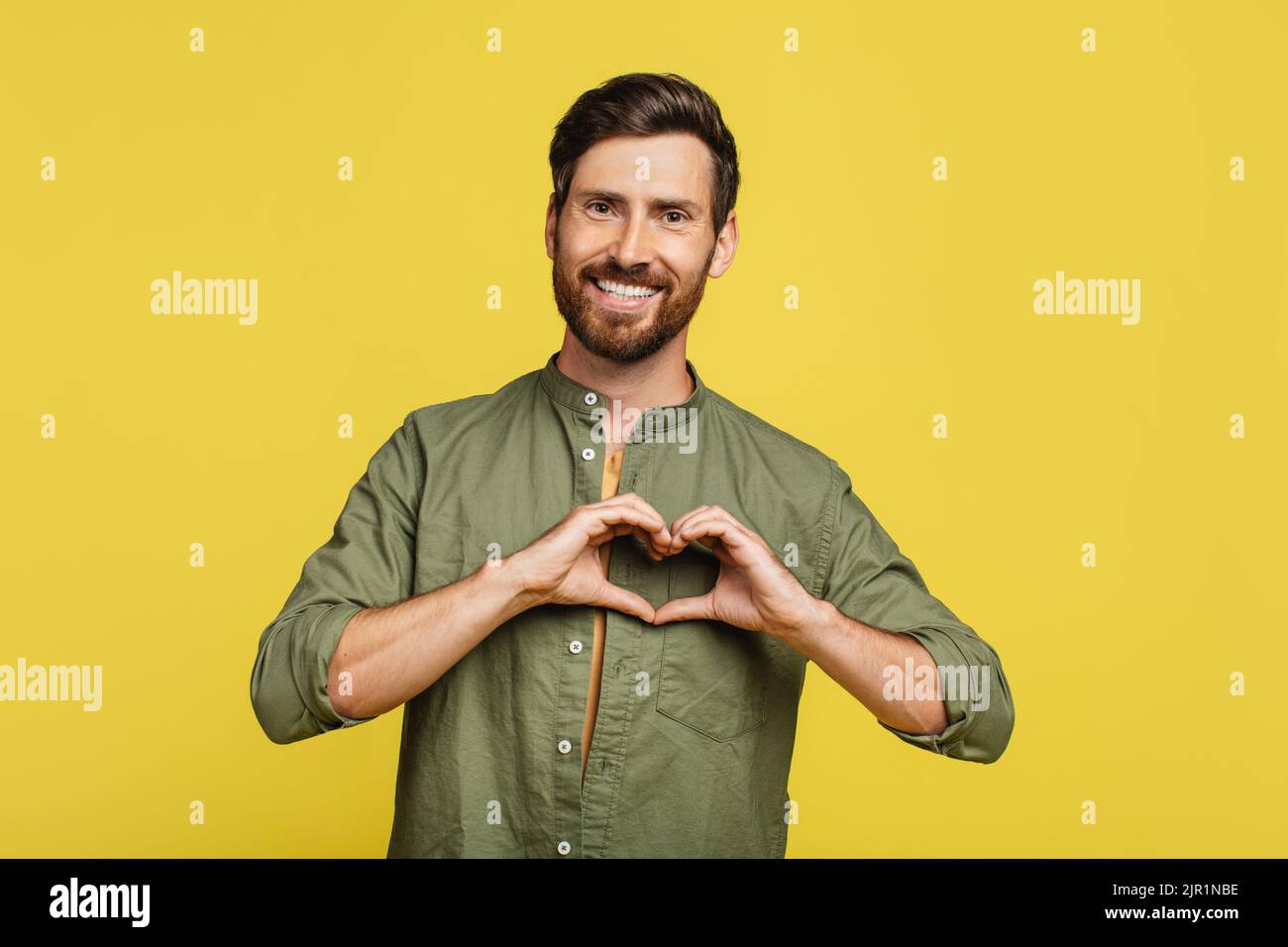 Kind man shaping hands like heart, making love gesture near chest, expressing kindness and smiling at camera Stock Photo