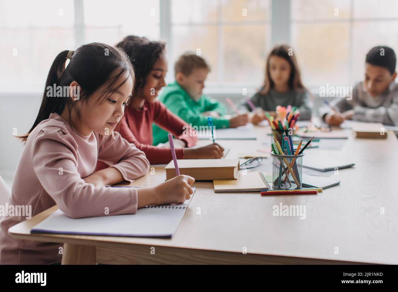 Asian Schoolgirl Taking Notes Learning Sitting In Modern Classroom Stock Photo