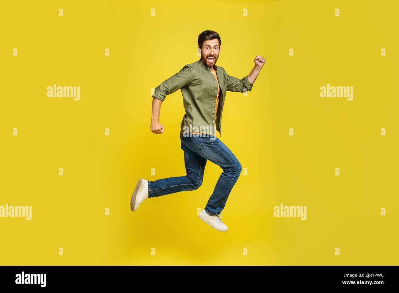 Portrait of middle aged man running over yellow background, side view shot of joyful male jumping in air Stock Photo