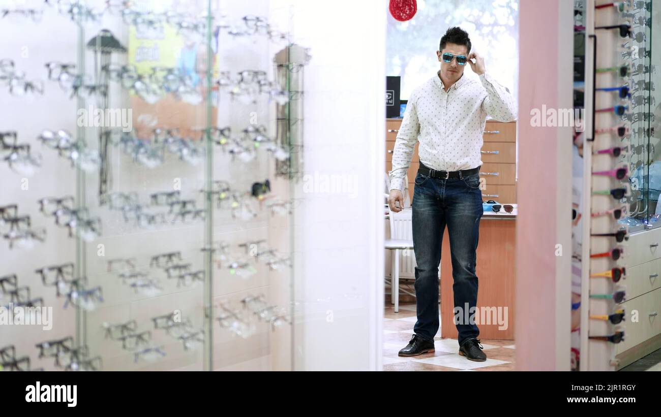 Handsome young man choosing eyeglasses in optical store. optics, optician retail store. health care, eyesight and vision concept . High quality photo Stock Photo