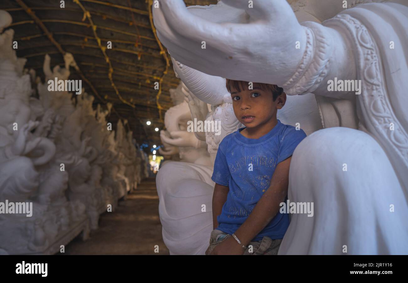 Pileru, India - July 28,2022:Young kid looking at camera and sitting on lord ganesha. Beautiful back ground with ganesha idols. Stock Photo