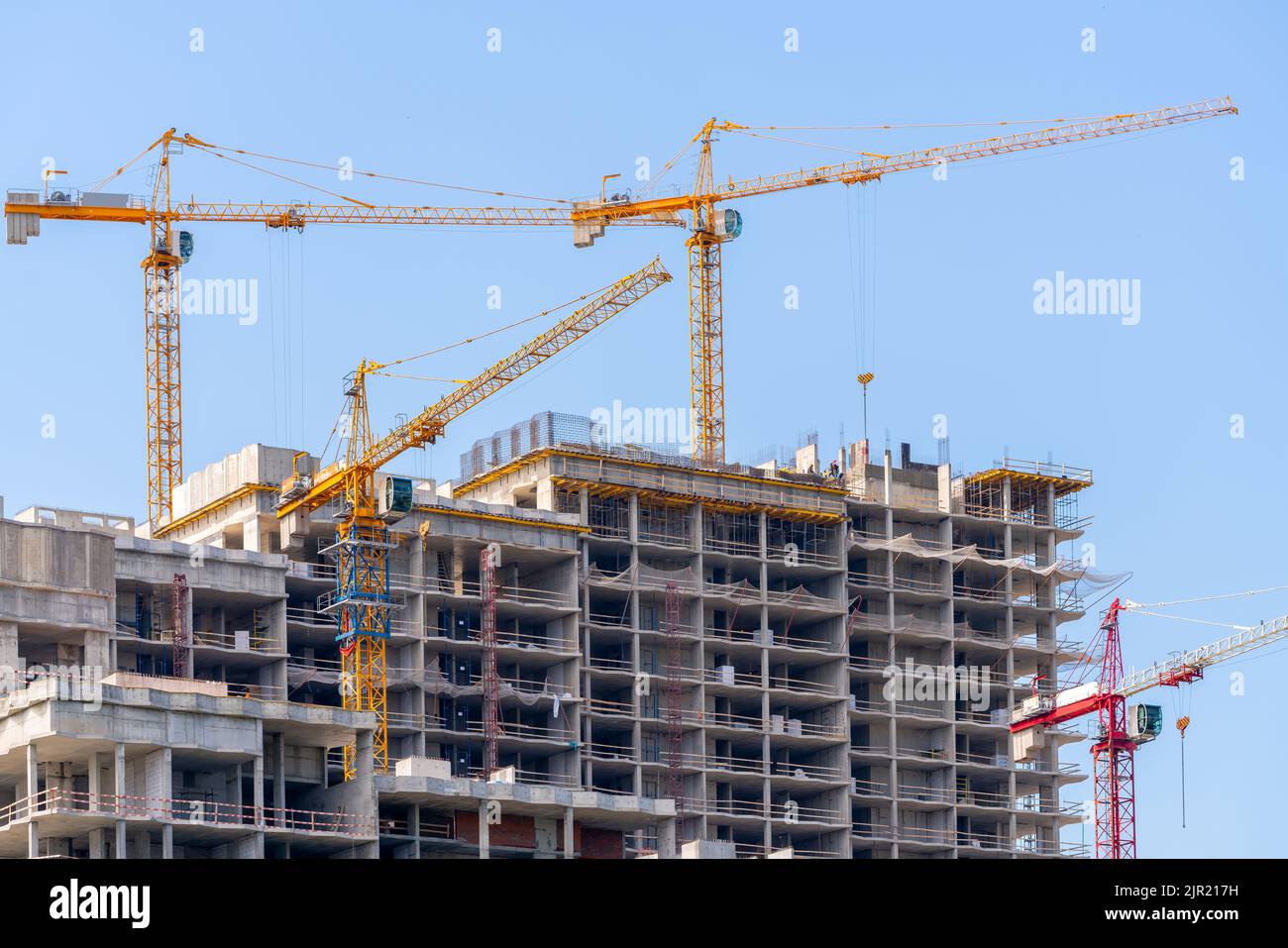 A low angle shot of cranes next to a buildings under construction ...