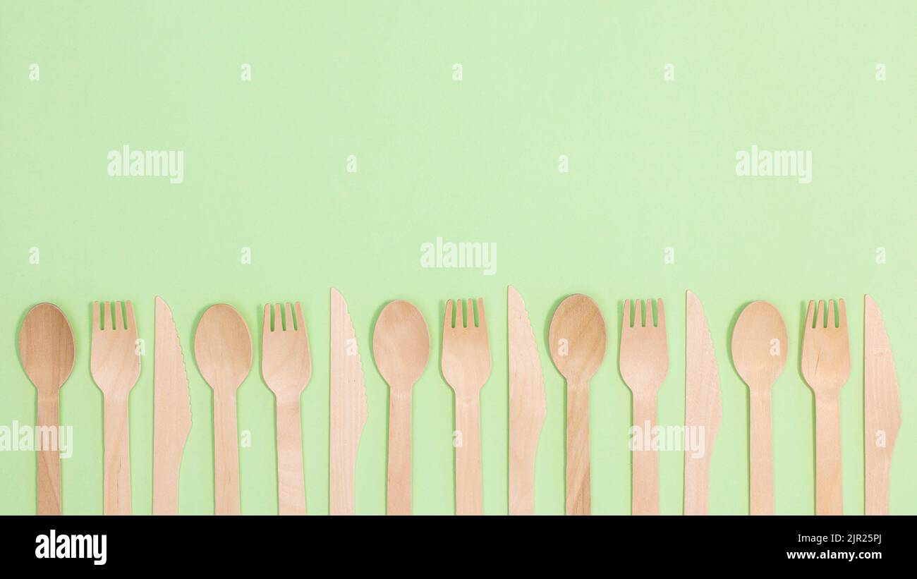 Wooden eco friendly spoons and forks on pastel green background. Flat