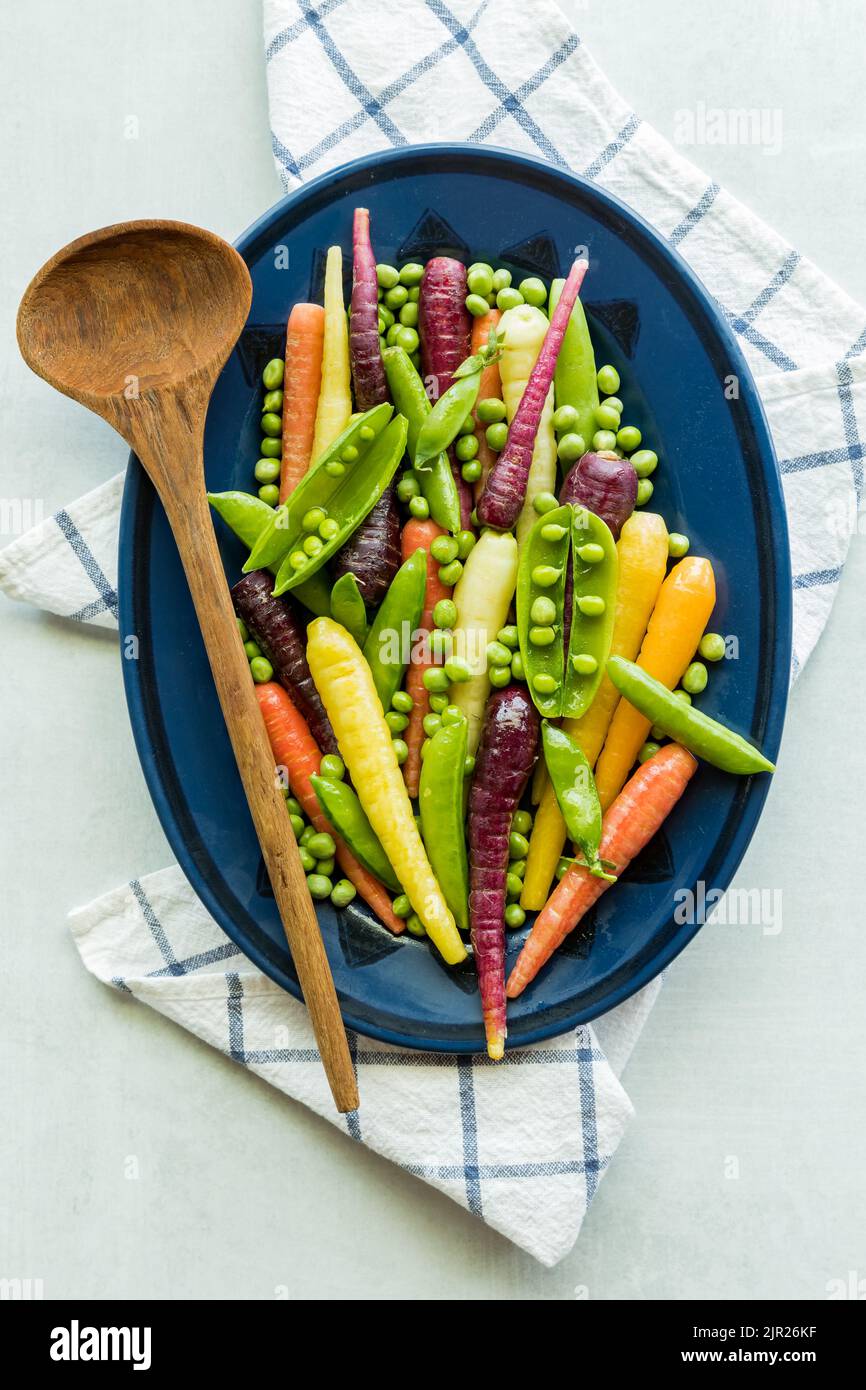 A medley of pea pods, peas and rainbow carrots on an oval plate Stock