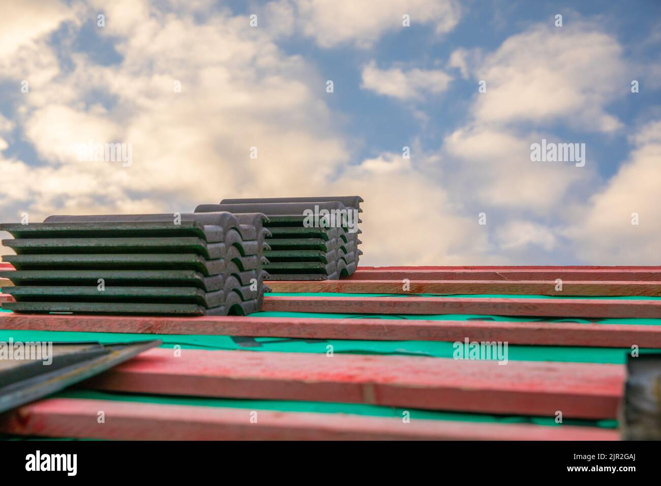 Piles of roof tiles on a bare roof with clouds behind Stock Photo