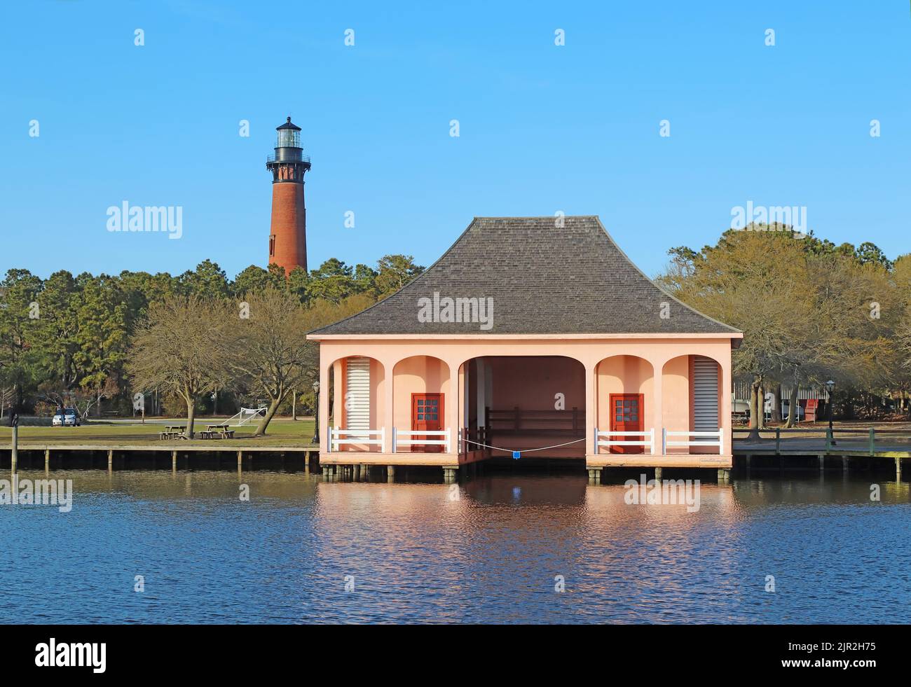 The red brick structure of the Currituck Beach Lighthouse rises over a pink boathouse in a historic park near Corolla, North Carolina Stock Photo