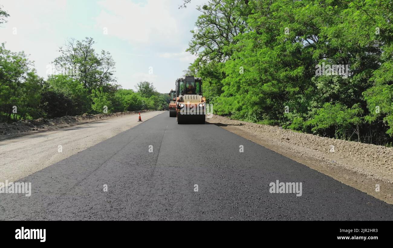repair of a highway, roller compactor machine and asphalt finisher laying a new fresh asphalt pavement, covering on one side of the traffic. Road construction works. High quality photo Stock Photo