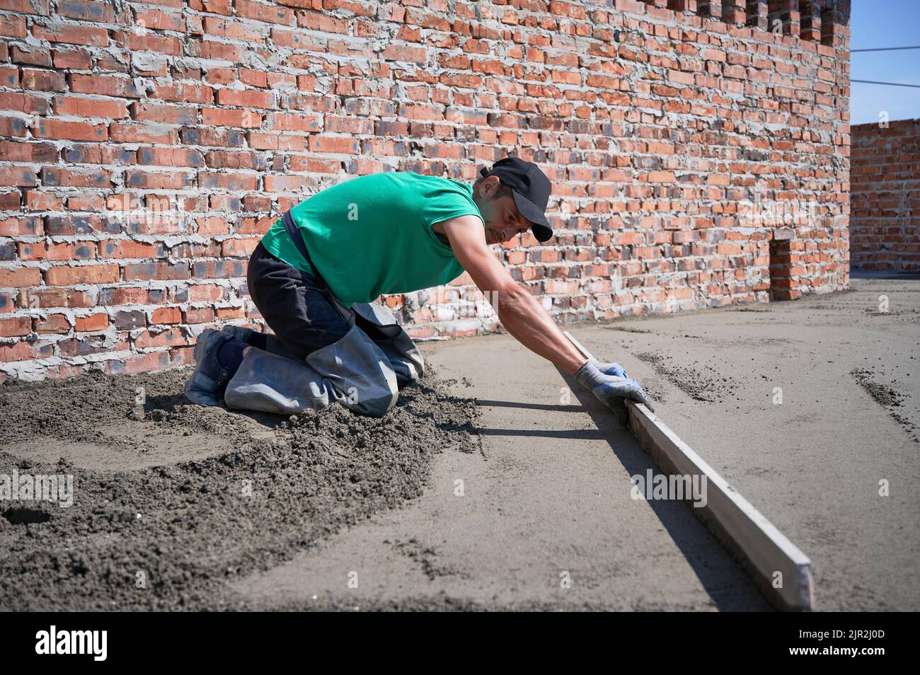 Side view of man in cap placing screed rail on the floor covered with