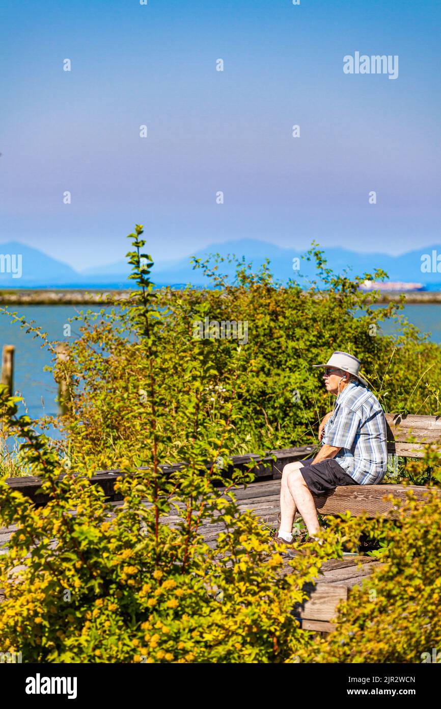 Older gentleman listening to music along the Steveston waterfront in British Columbia Canada Stock Photo