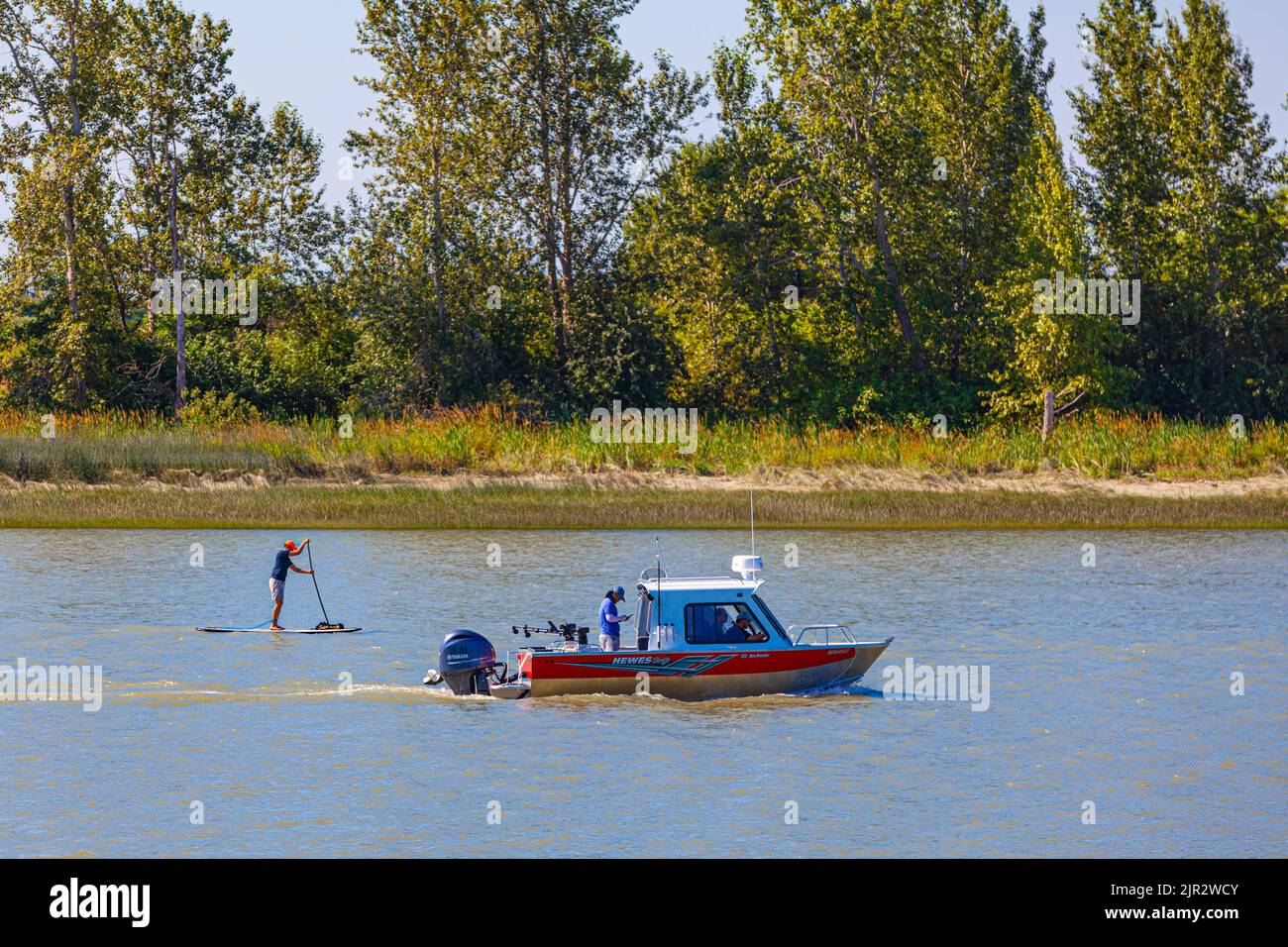 Power boat and Paddle boarder heading down the Steveston channel in British Columbia Canada Stock Photo