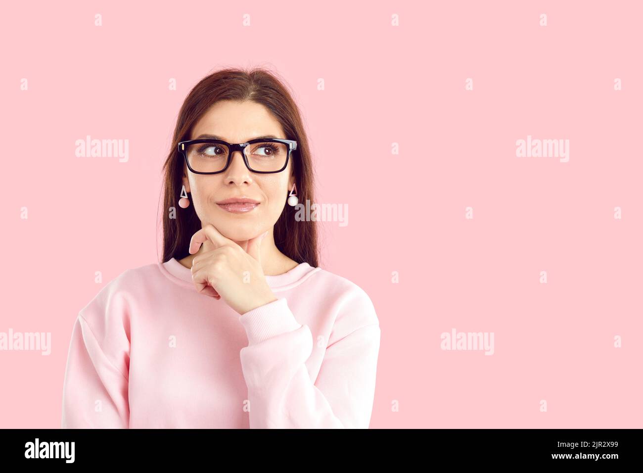 Young Caucasian woman wearing glasses coming up with new idea, touching chin looking to side Stock Photo