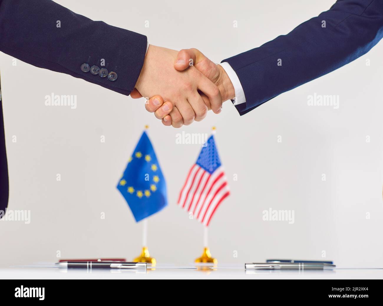 Two diplomats or politicians from USA and European Union shake hands at negotiation table Stock Photo