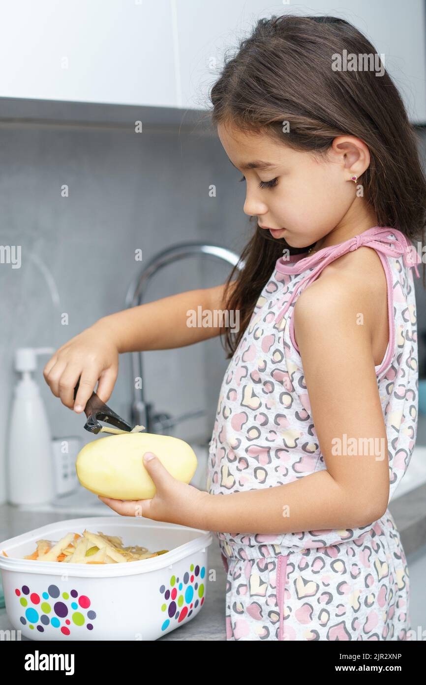 Boy using peeler to peel raw potato available as Framed Prints