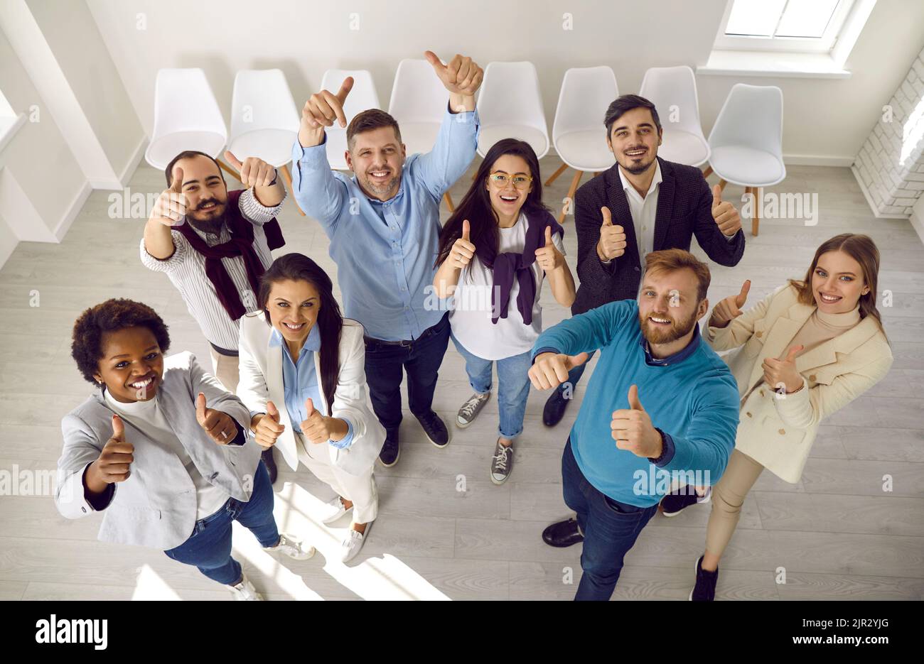 Team of people who make happy gesture by raising their hands with thumbs up demonstrating success. Stock Photo
