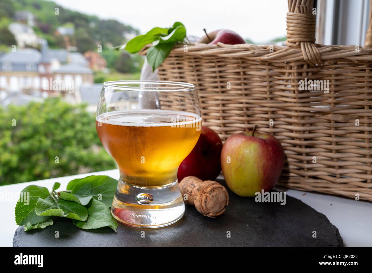 Glass of cold apple cider drink, ripe apples with leaves and houses of
