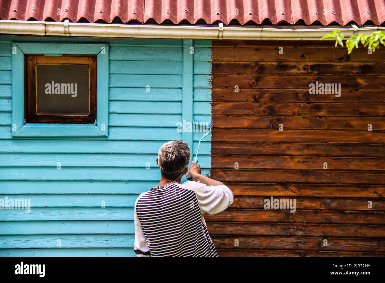 A view of a male painting a wooden house in blue Stock Photo Alamy