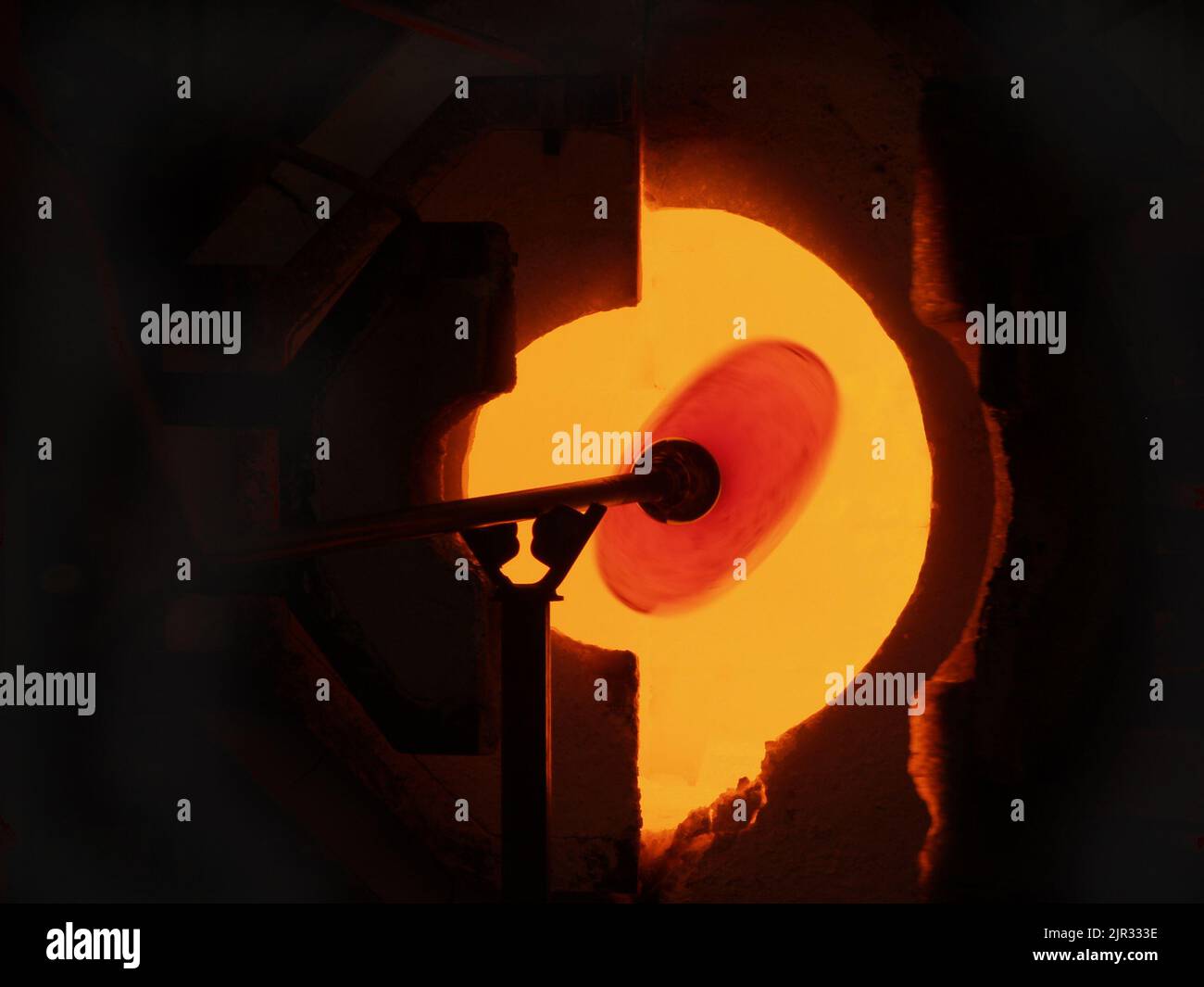 Hot molten glass illuminated by the glow of fire through opening in