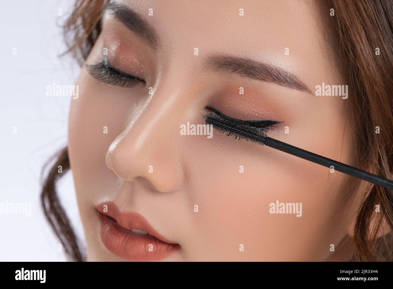 Closeup gorgeous young woman putting black mascara on her long eyelashes with brush. Beauty cosmetic concept. Female model with perfect skin. Stock Photo