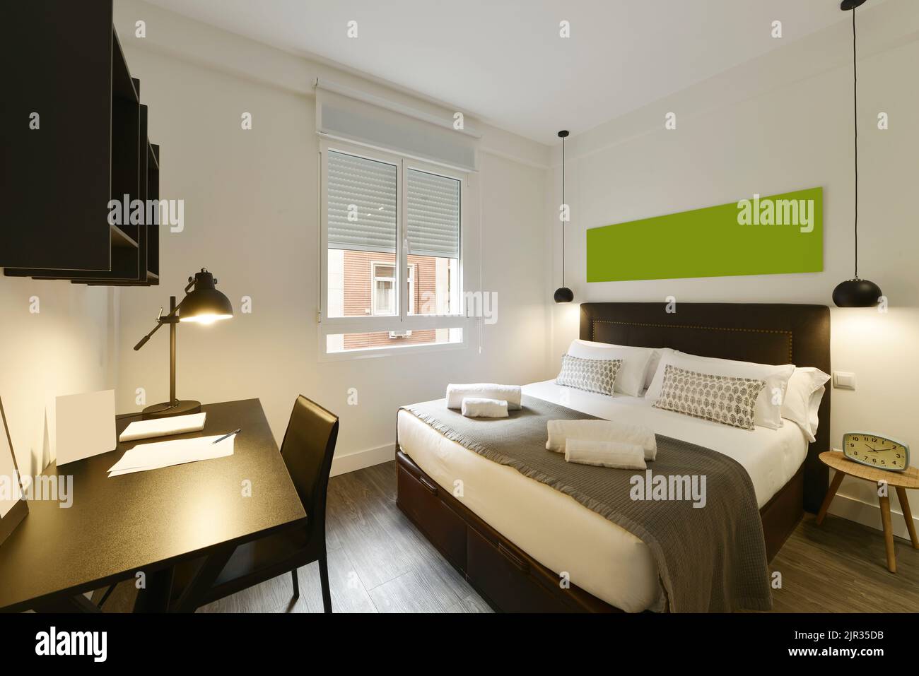 Bedroom with double bed, headboard upholstered in dark brown fabric, wooden floor and desk with