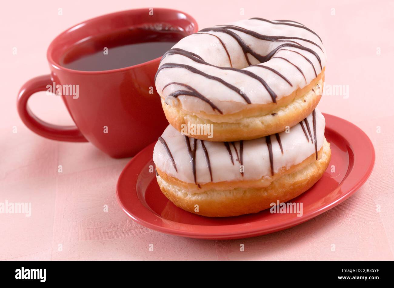 Glazed sweet doughnuts on red saucer and a cup of tea Stock Photo