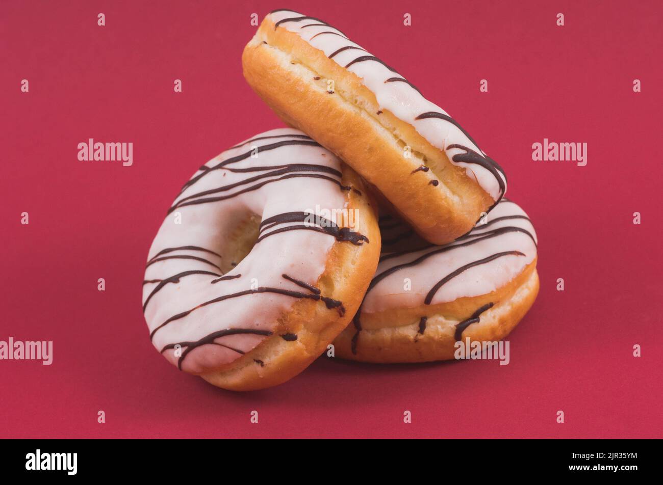 Three glazed sweet doughnuts on red background Stock Photo