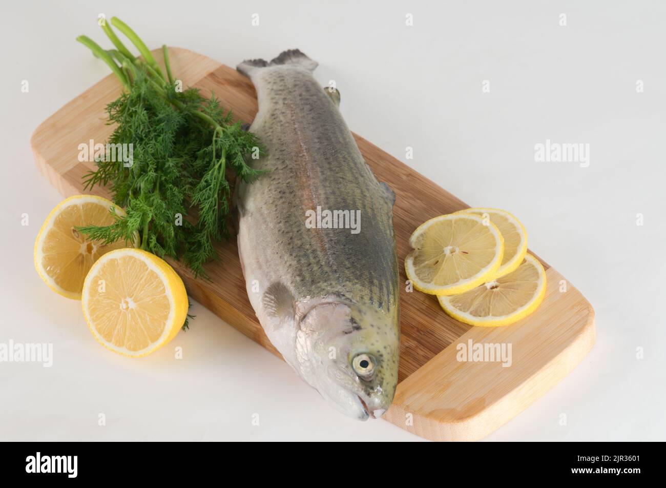 Raw trout on a wooden cutting board with sliced lemon and fresh dill Stock Photo