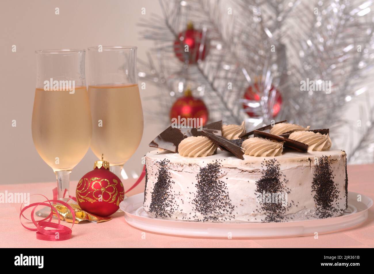 Christmas cake and two glasses of white wine on a Christmas table against decorated silver Christmas tree Stock Photo