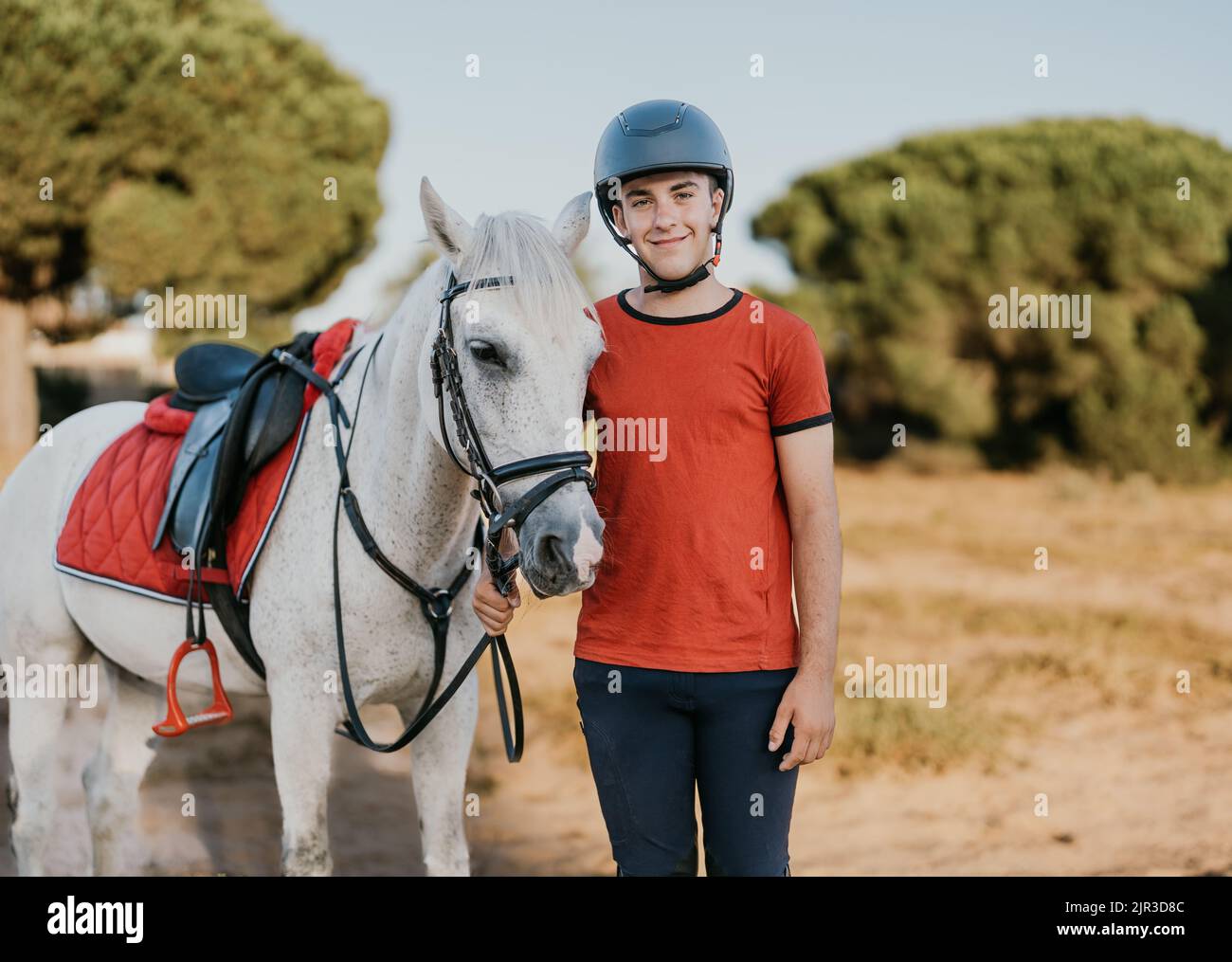 portrait of young smiling rider standing next to his white horse in a ...
