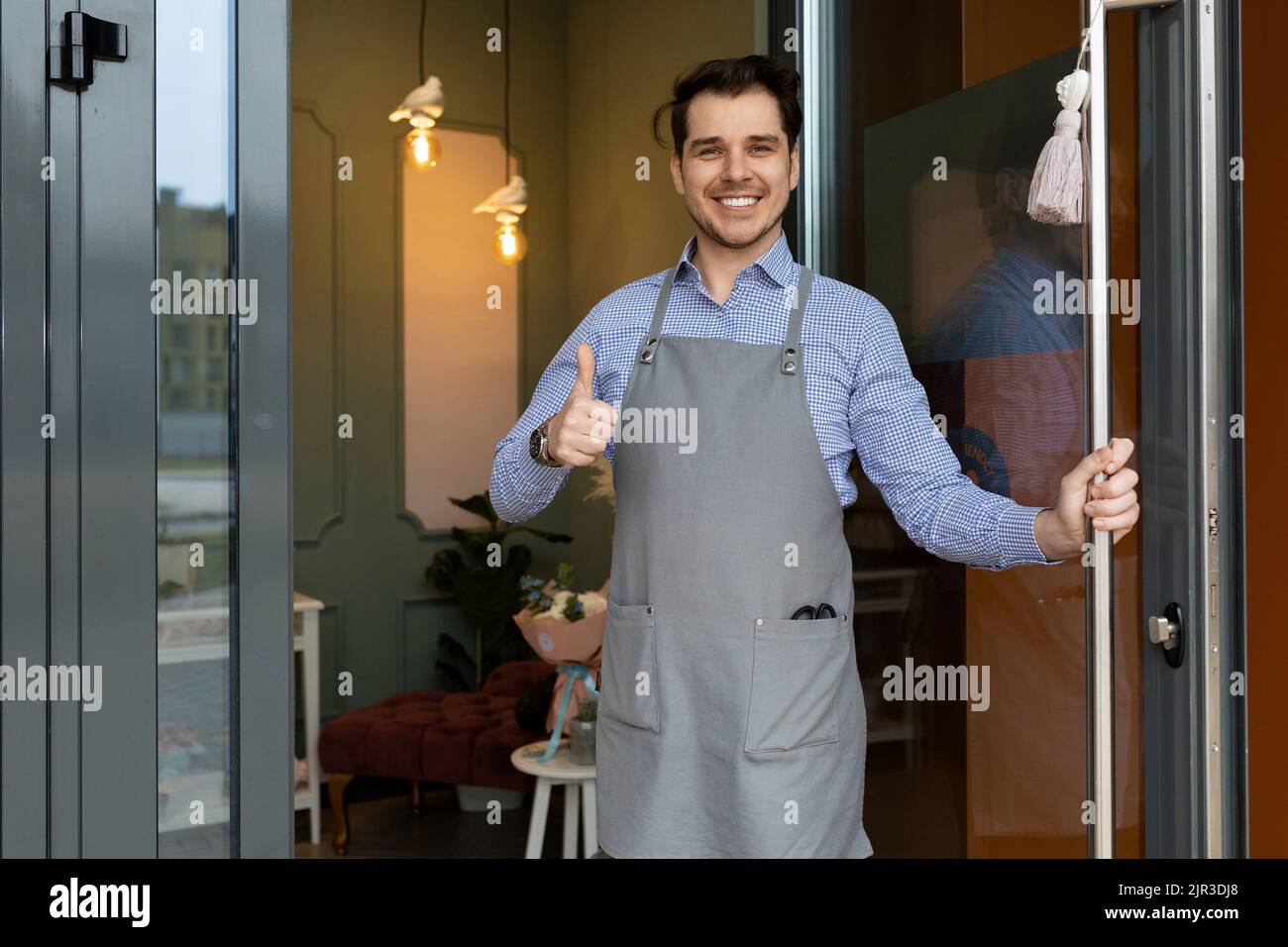 the owner of a cozy establishment kindly and cordially meets his clients on the threshold of the establishment by opening the door Stock Photo