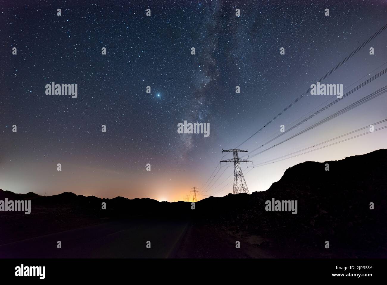 A scenic view of power towers and lines on a hill under a starry night ...