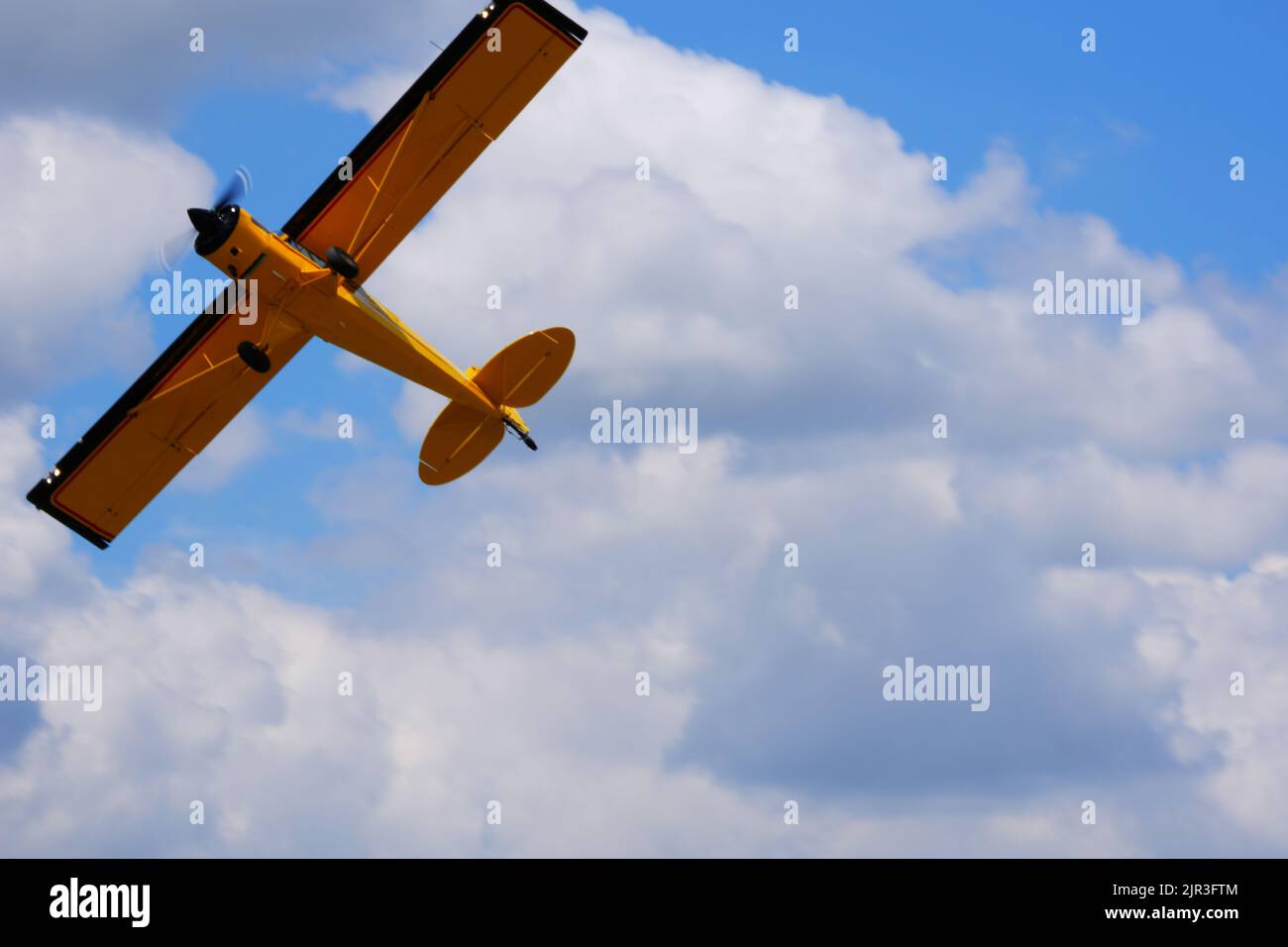 Single engine yellow propeller air plane flying at cloudy blue sky in a summer day Stock Photo