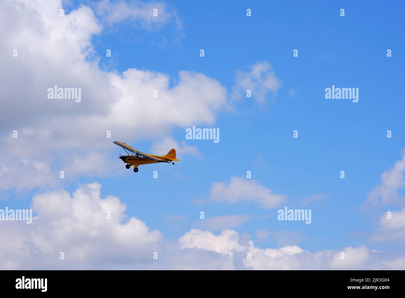Single engine yellow propeller air plane flying at cloudy blue sky in a summer day Stock Photo