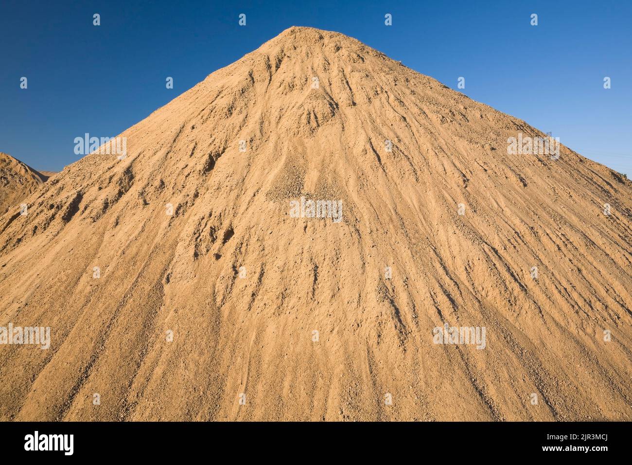 Large mound of stacked tan colored sand in a commercial sandpit. Stock Photo